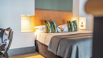 Een keurig opgemaakt bed met kussens, een bedlampje en een stoel in een hotelkamer.