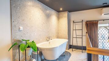 A modern bathroom with a freestanding bathtub, a potted plant, and a towel rack.