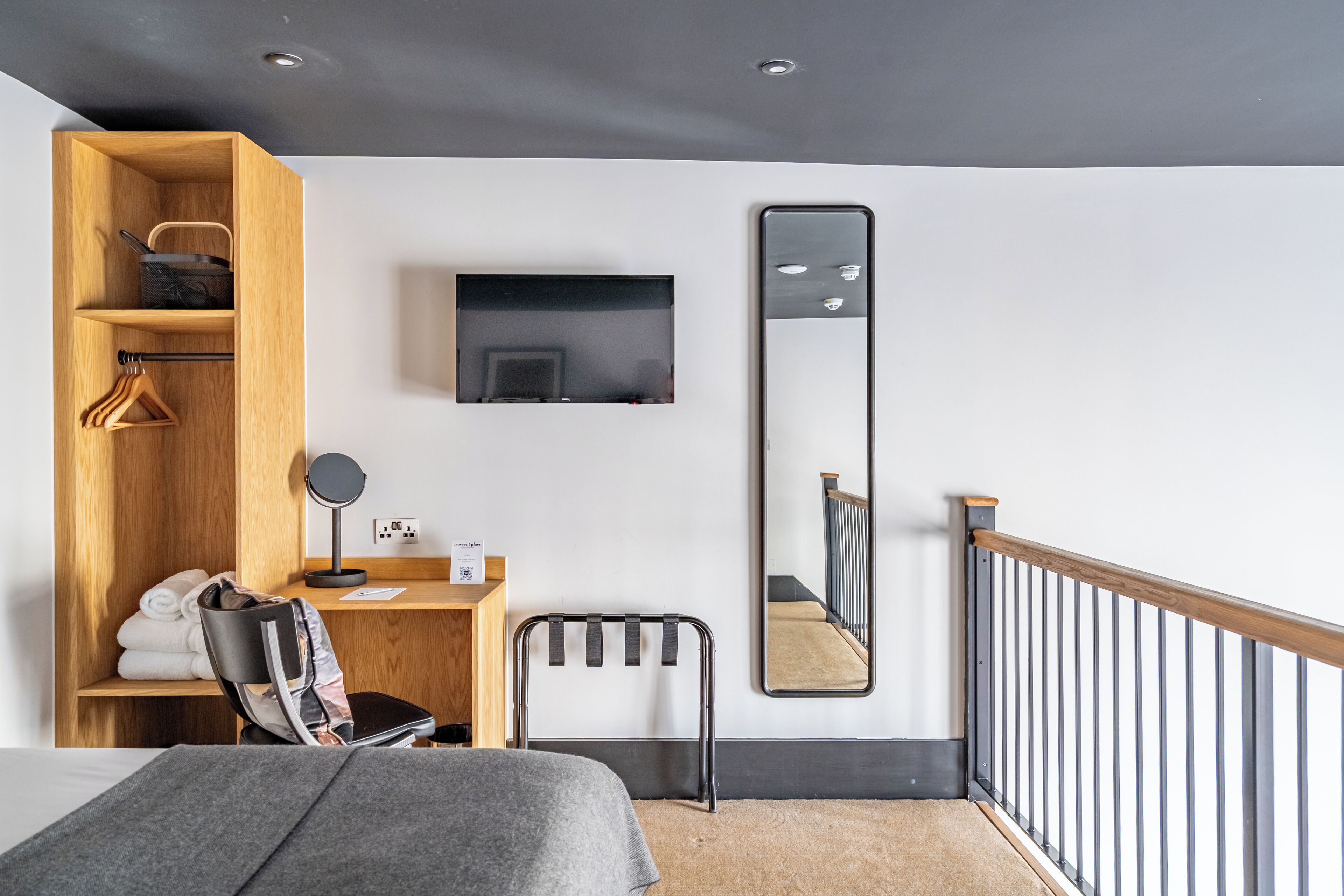 A modern bedroom with a bed, a desk, a chair, a TV, a mirror, and a wardrobe.