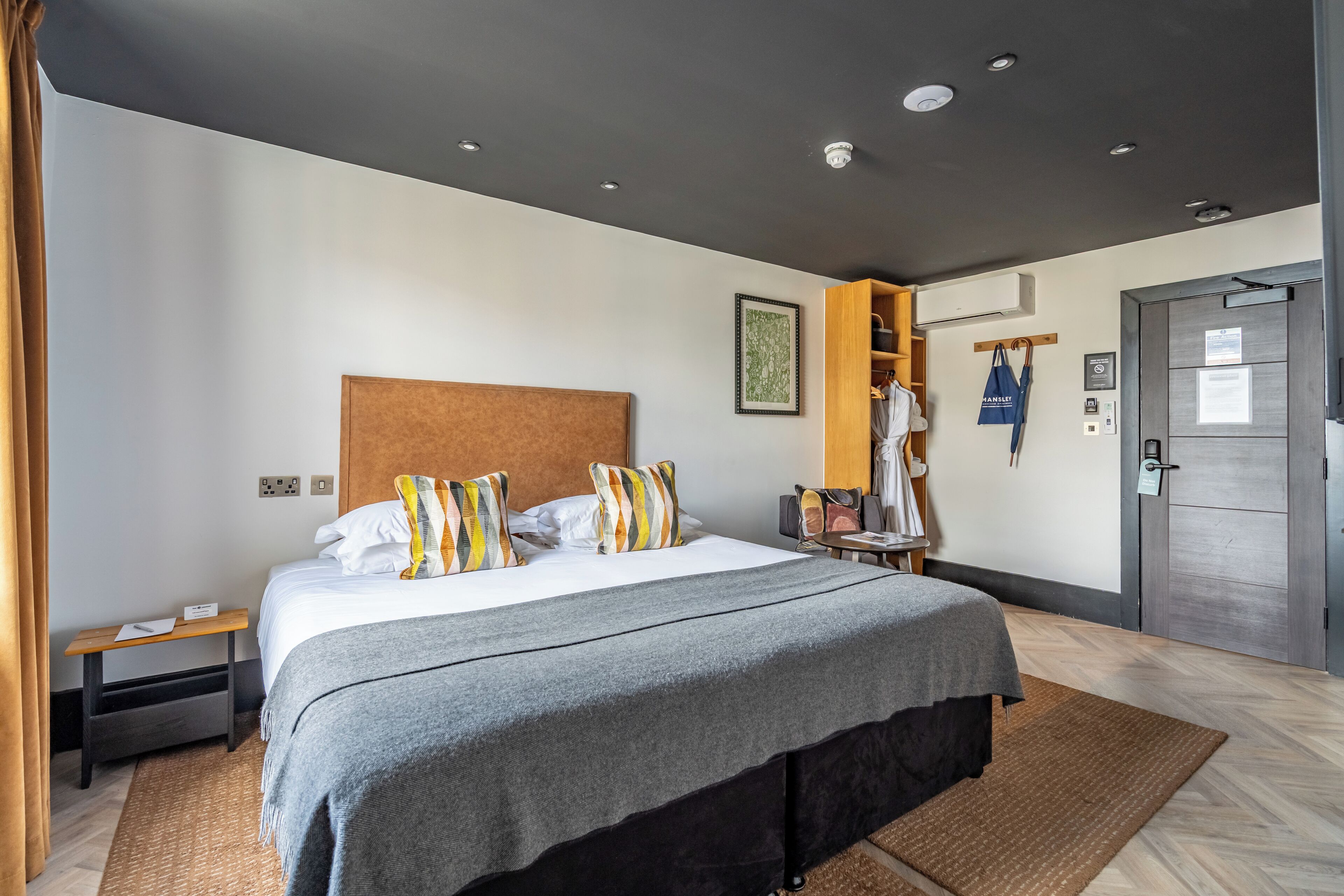 A modern hotel room with a large bed, a wooden headboard, a wardrobe, and a door with a handle.
