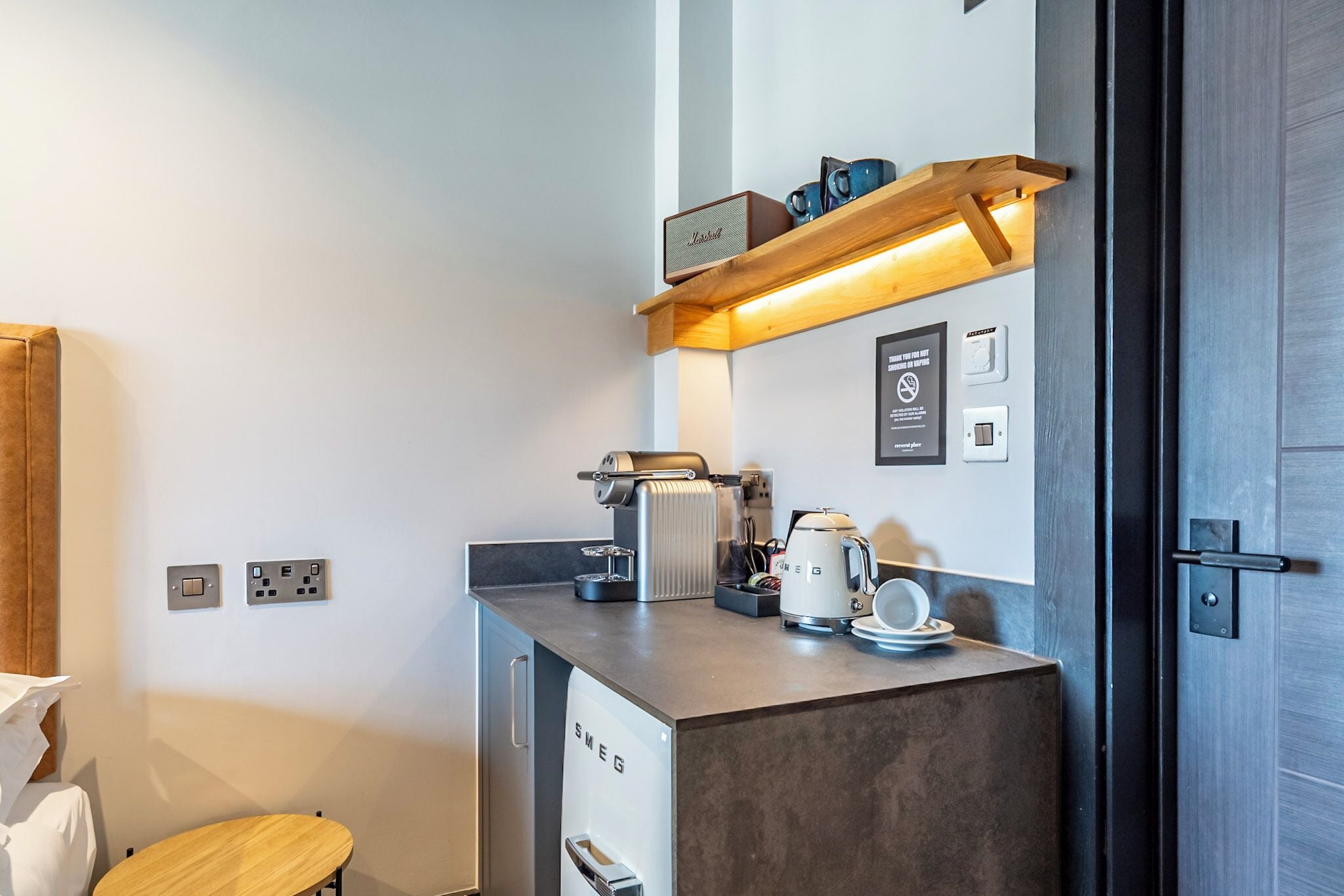 A compact kitchenette with a coffee maker, a kettle, and a shelf with mugs.