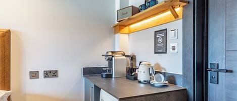 A compact kitchenette with a coffee maker, a kettle, and a shelf with mugs.