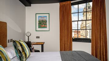 A hotel room with a bed, a desk, a mirror, and a window with curtains.