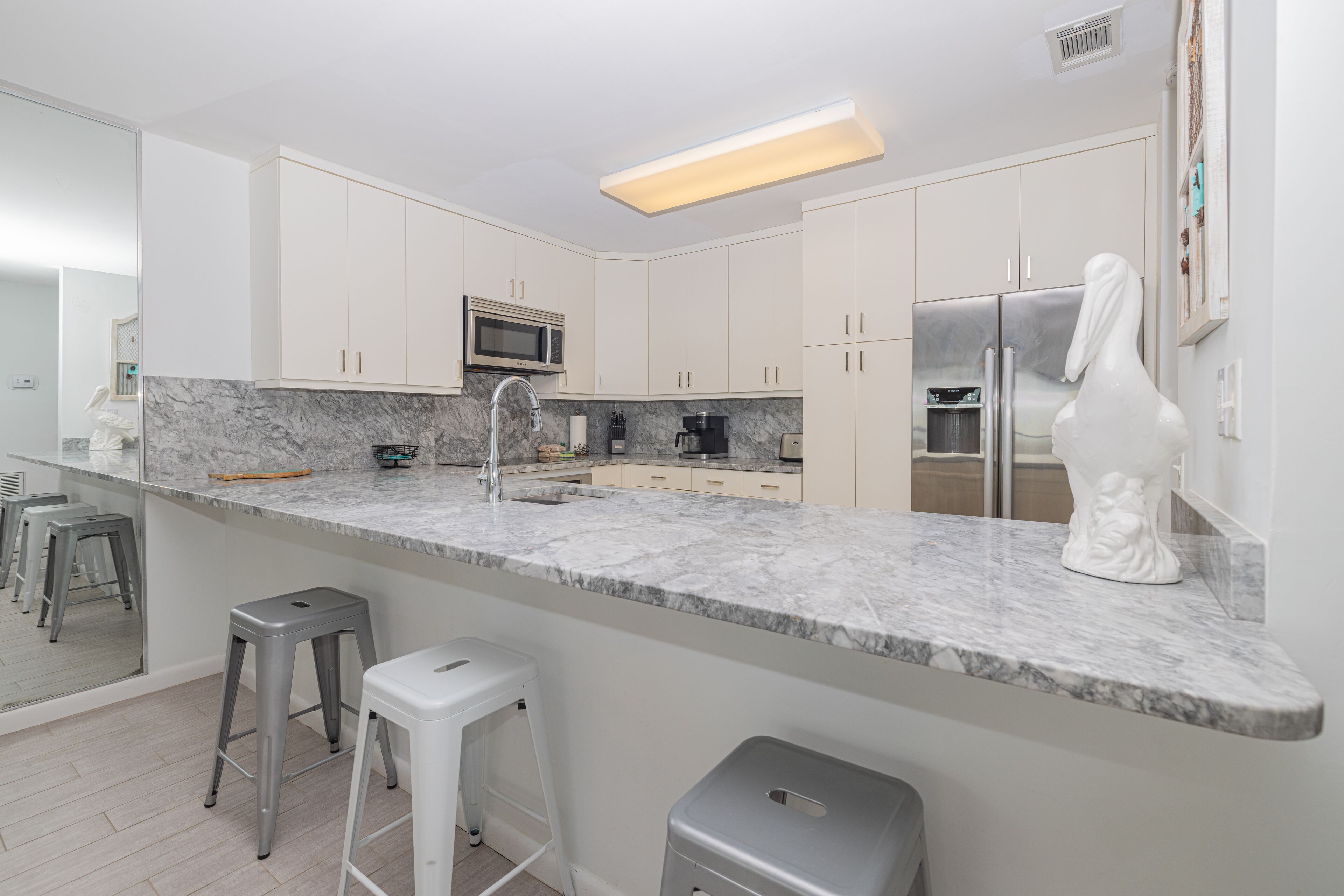 A modern kitchen with white cabinets, a marble countertop, a stainless steel refrigerator, and a white statue.