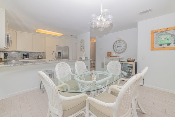 A modern kitchen with white cabinetry, a glass dining table, wicker chairs, and a chandelier. - Oceanfront Condo in Wild Dunes! Community Pool! Great View Looking at Ocean! (Isle Of Palms)