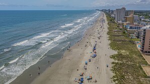 A beach with a long stretch of sand, a few umbrellas, and buildings along the shore.