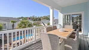 A covered outdoor area with a pool, wicker furniture, and a view of neighboring houses.
