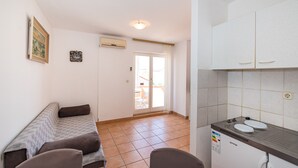 Een ruimtelijk ingerichte woonruimte met kitchenette, een bank, een eethoek en een glazen schuifdeur naar buiten.