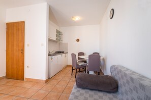 A compact living space with a kitchenette, a dining area with a table and chairs, and a sofa with a cushion. - Apartment Near Supermarket Milo (Novalja)
