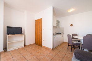 A compact living space with a television on a shelf, a wooden door, a kitchenette, and a dining area with chairs. - Apartment Near Supermarket Milo (Novalja)