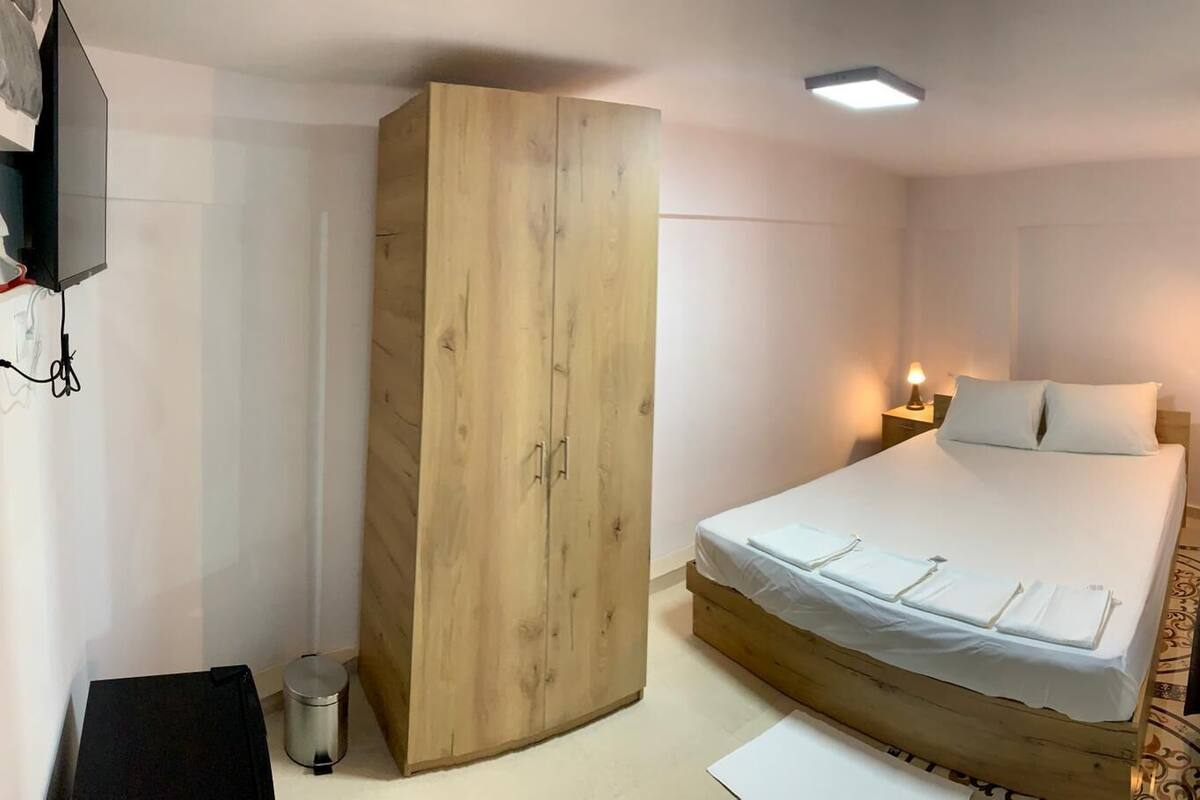 A bedroom with a bed, a wardrobe, a desk, and a lamp.