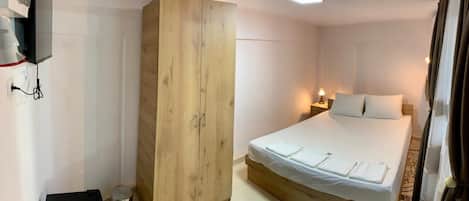 A bedroom with a bed, a wardrobe, a desk, and a lamp.
