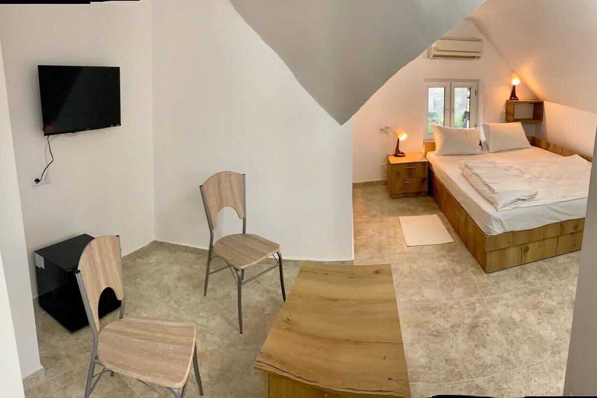 A bedroom with a bed, bedside tables, a chair, a TV, and a window.