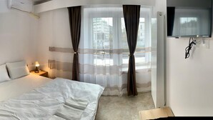 A hotel room with a bed, bedside tables, a wooden wardrobe, a TV, and a window with curtains. - Hostel Jaz (Bucharest)
