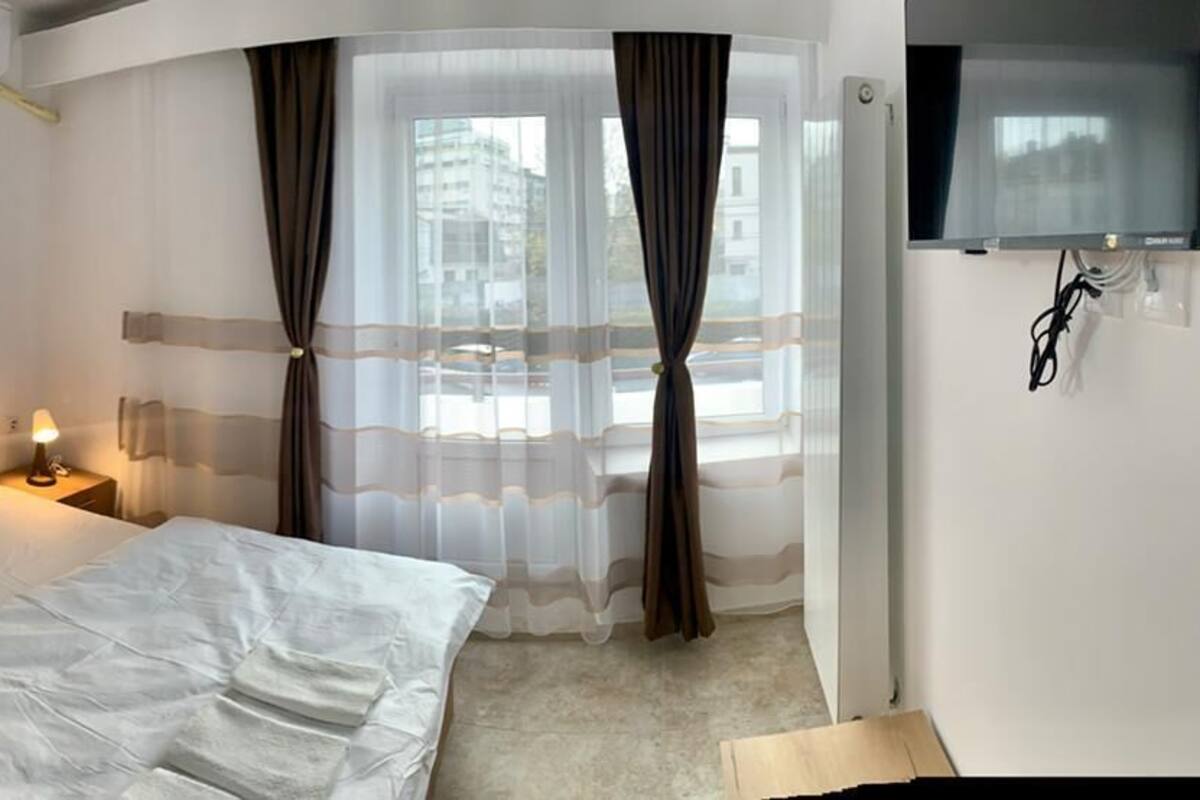 A hotel room with a bed, bedside tables, a wooden wardrobe, a TV, and a window with curtains.
