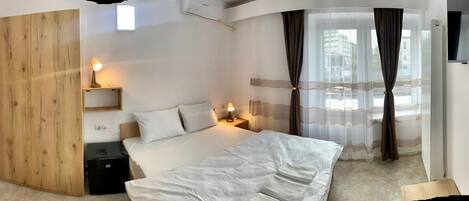 Habitación de hotel con cama, mesitas de noche, armario de madera, televisor y ventana con cortinas.