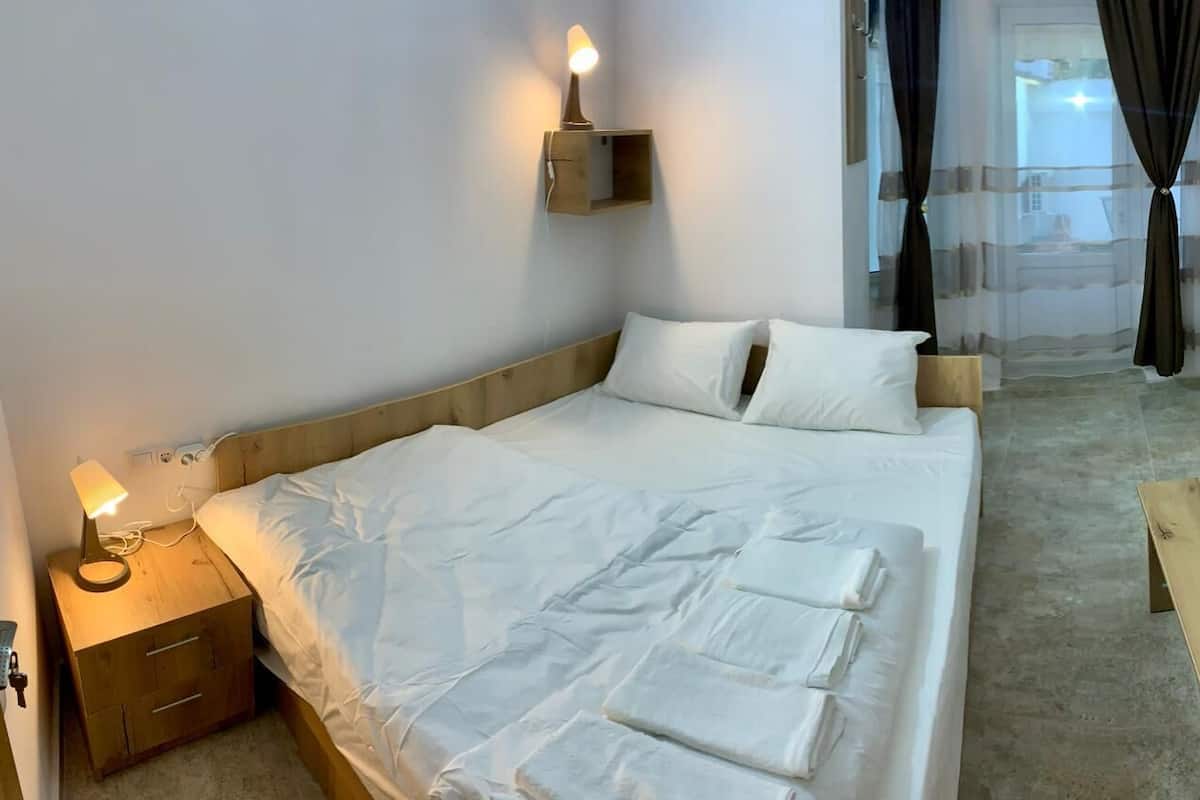 A neatly made bed with white linens, a bedside lamp, and a wooden nightstand with a drawer.