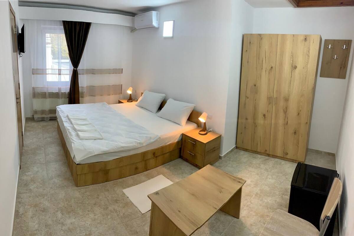 A bedroom with a wooden bed, bedside tables with lamps, a wooden wardrobe, and a small wooden table.