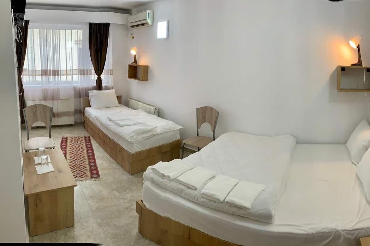 A hotel room with two single beds, a desk, a chair, and a small table.