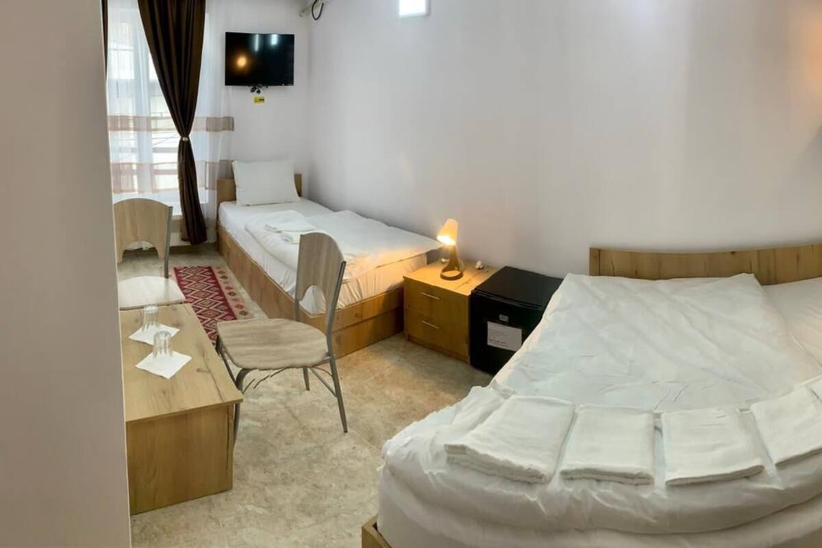 A hotel room with a large bed, a desk with a chair, a TV, and a bedside table with a lamp.