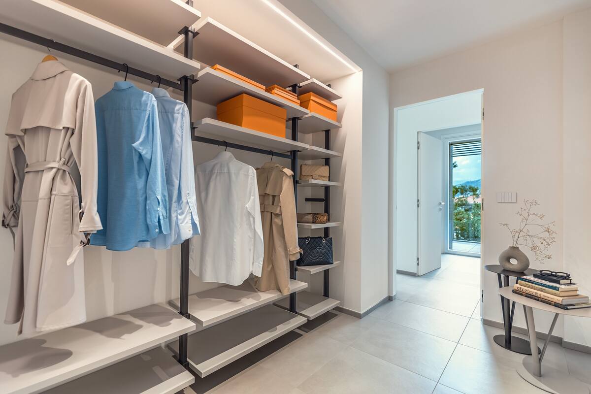 A modern closet with shelves and hanging space, a small table with books and a vase, and a view of the outdoors through an open door.
