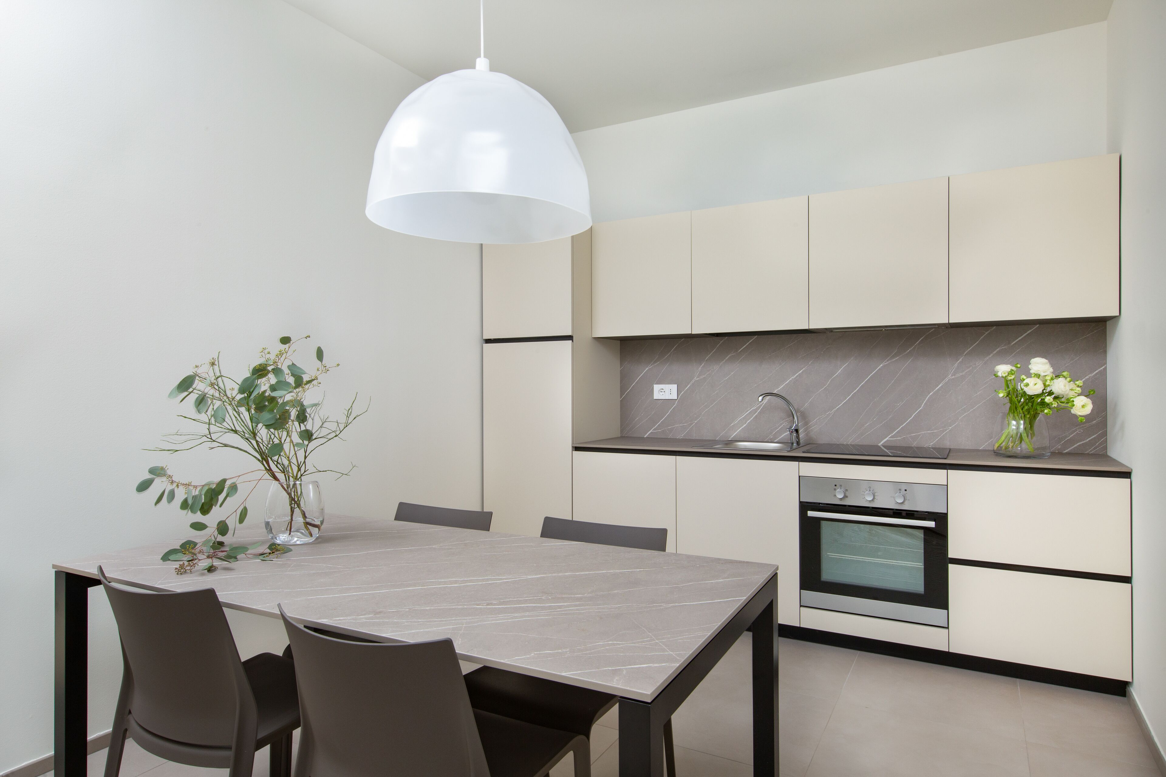 A modern kitchen with a marble countertop, built-in oven, and a dining area with a table and chairs.
