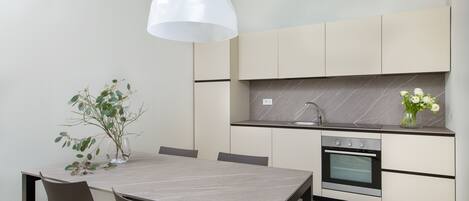 A modern kitchen with a marble countertop, built-in oven, and a dining area with a table and chairs.