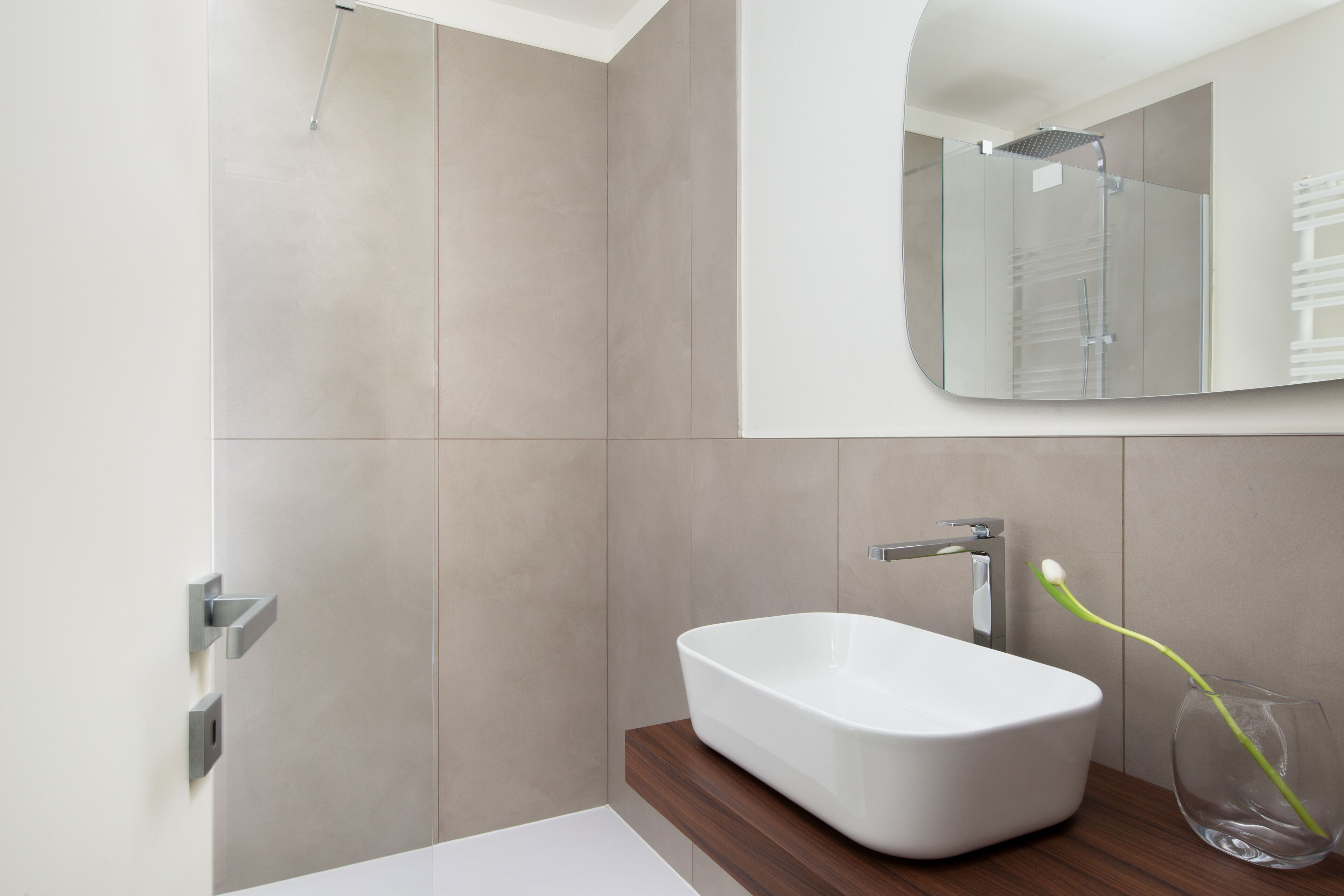 A modern bathroom with a white sink, a glass shower enclosure, and a wooden vanity.