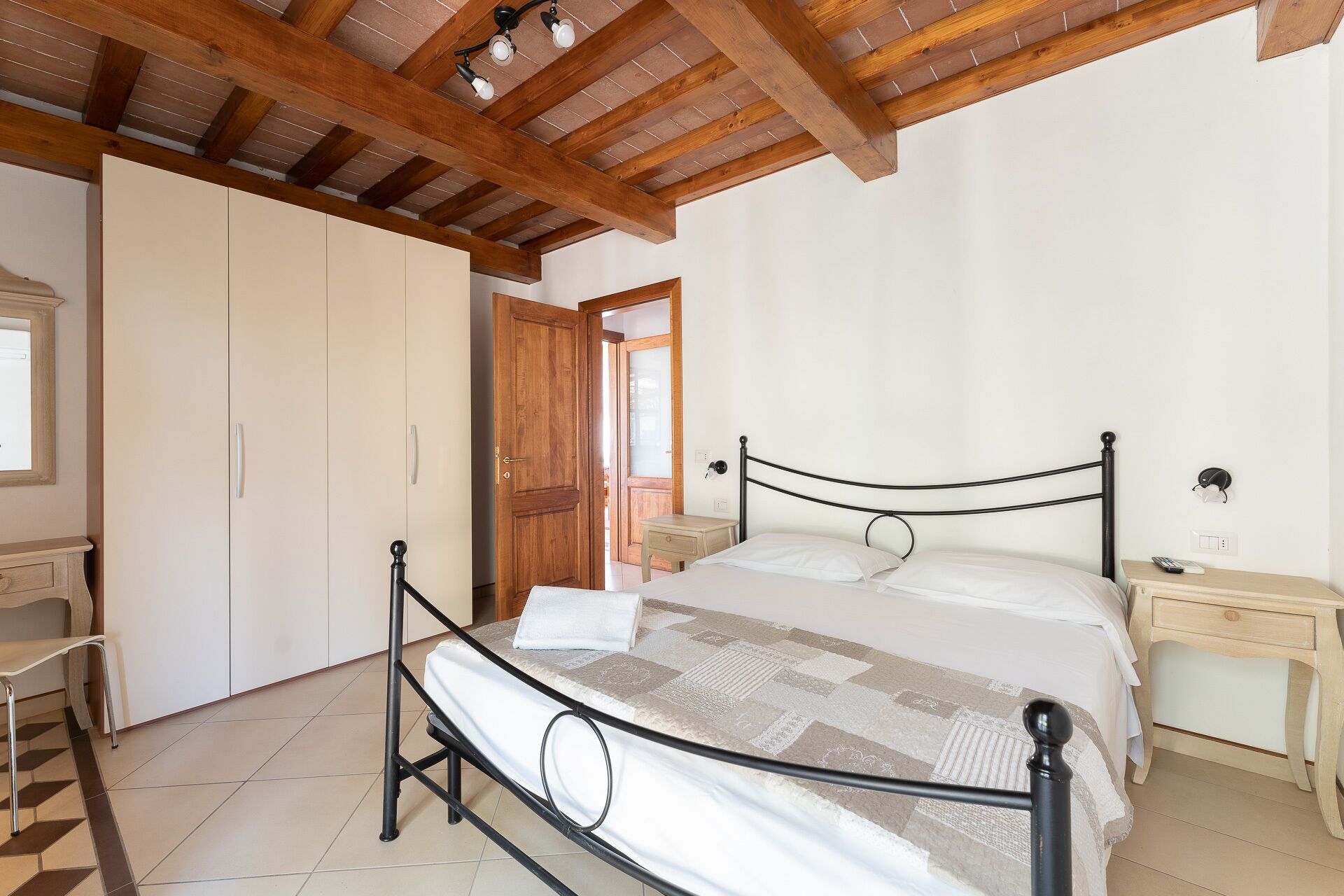 Un dormitorio con cama, vigas de techo de madera, armario, mesita de noche y escritorio.