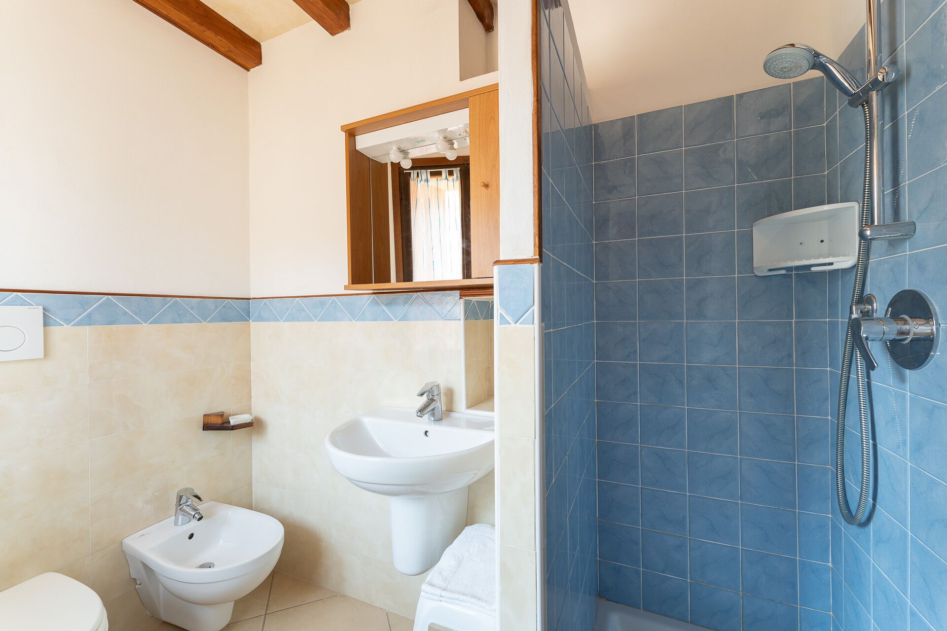 A bathroom with a bidet, a sink, and a shower with blue tiles.