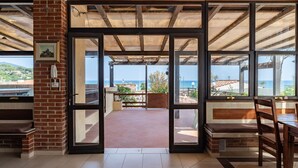 A room with a large glass door leading to an outdoor terrace with a view of the sea. - Hotel Delfino (Marciana)