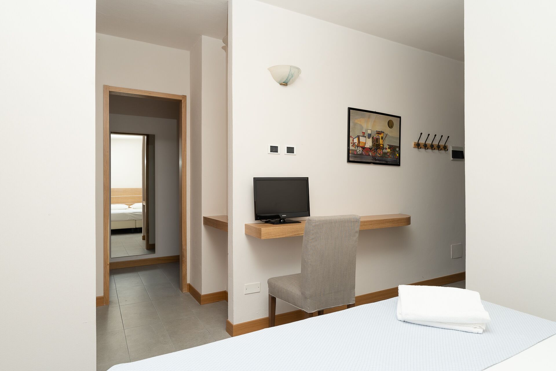 Habitación de hotel con cama, escritorio con ordenador, silla, luz adosada a la pared y un cuadro.