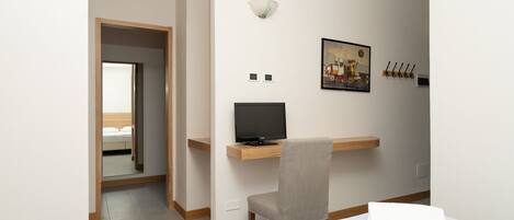Habitación de hotel con cama, escritorio con ordenador, silla, luz adosada a la pared y un cuadro.