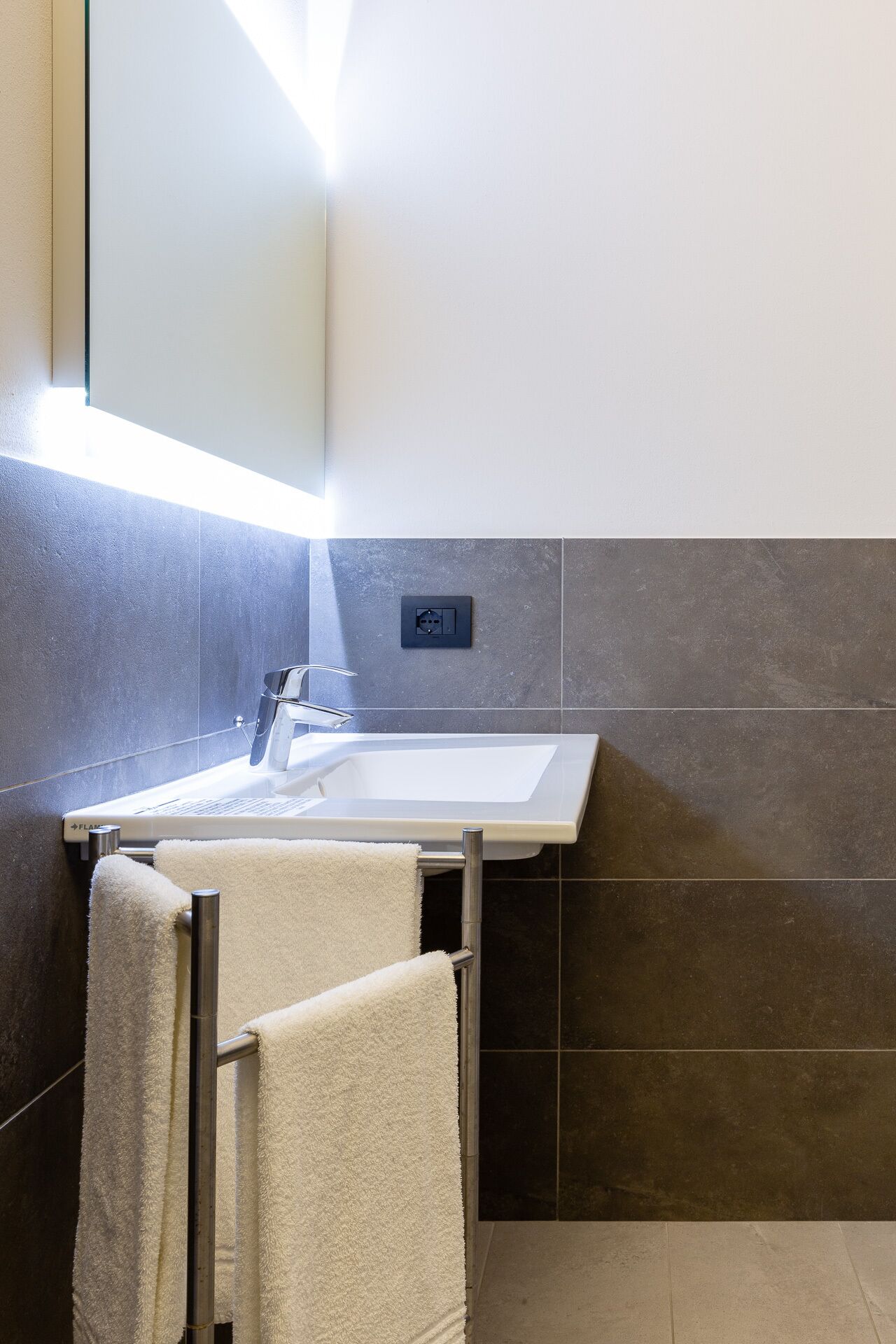 Une salle de bain moderne avec un lavabo blanc, un miroir et un porte-serviettes.
