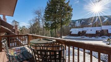 Une terrasse en bois avec une table et des chaises, un paysage enneigé et une montagne en arrière-plan.