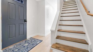 A staircase with wooden steps and a handrail, leading to a door with a dark gray finish and a patterned doormat.