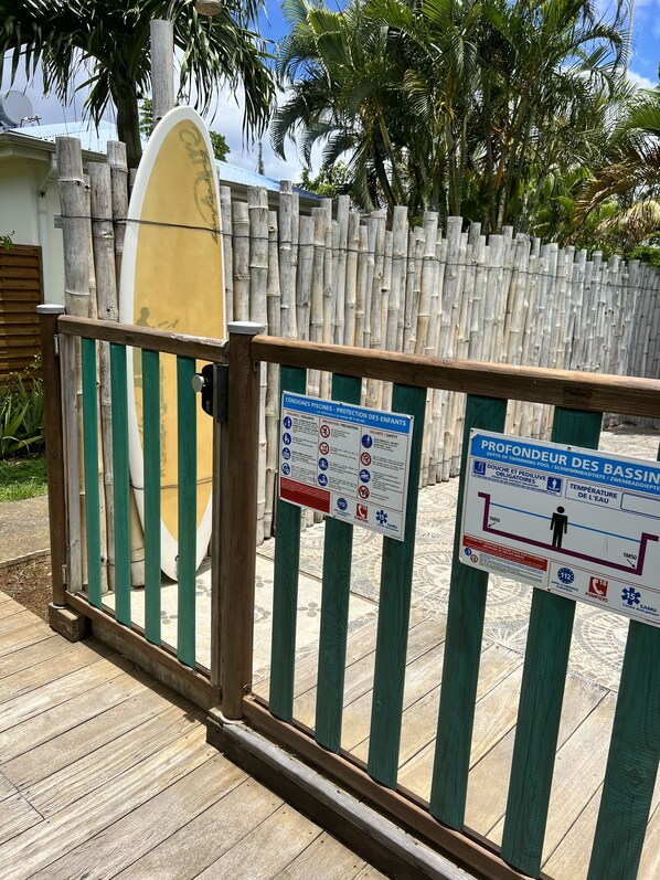 Un cancello di legno con una tavola da surf e cartelli di sicurezza.
