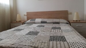 Ein ordentlich bezogenes Bett mit einem gemusterten Quilt, zwei Nachttischlampen und einem Bild an der Wand.