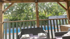 A covered outdoor seating area with a view of a swimming pool and lush greenery.