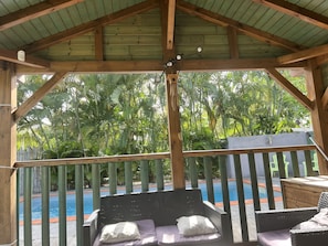 Un espace extérieur aménagé, abrité et doté de sièges, offrant une vue sur une piscine et une végétation luxuriante.