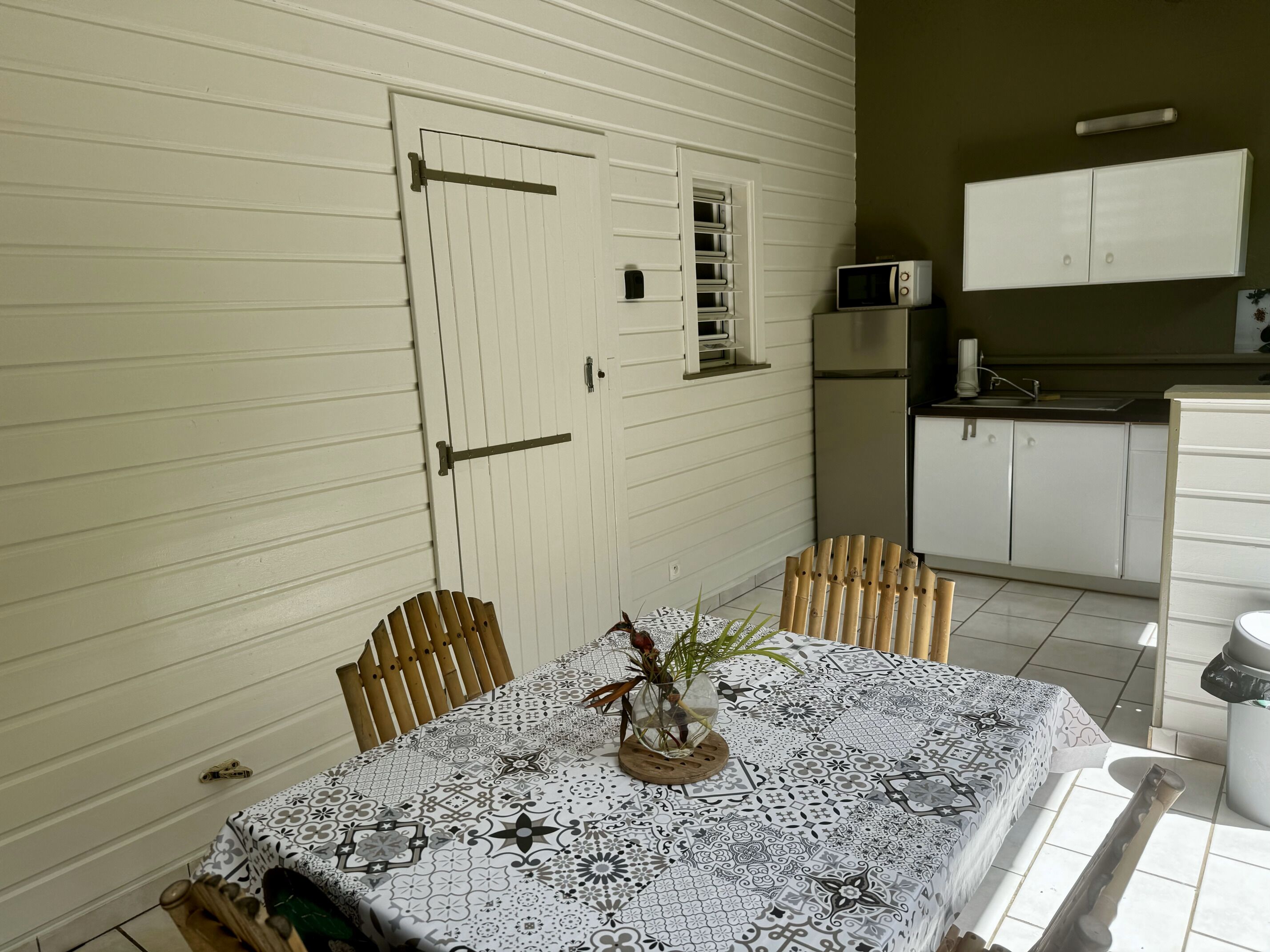 Uma sala de jantar com mesa posta para dois, uma porta e área de cozinha com armários e eletrodomésticos.