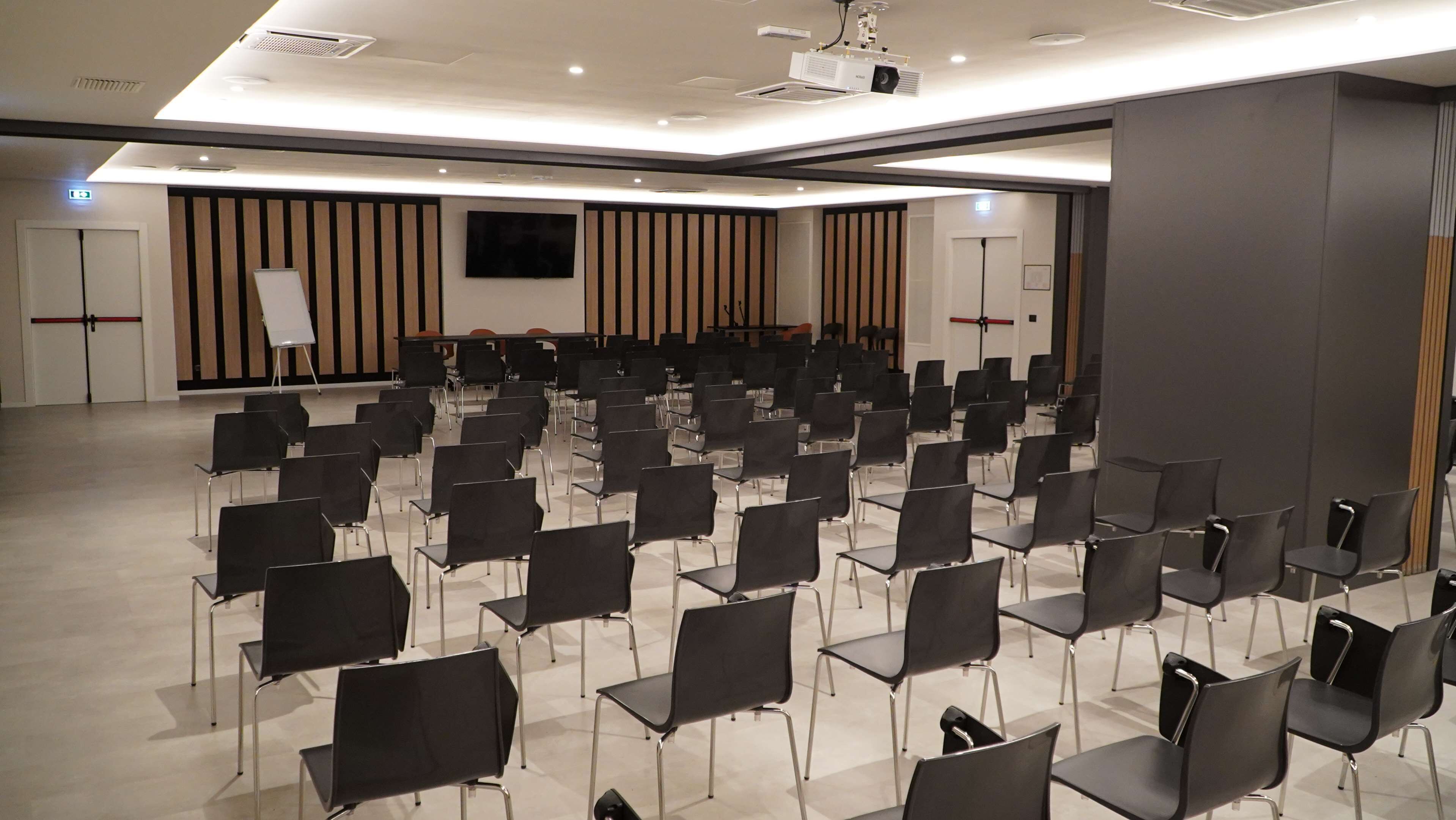 A conference room with rows of black chairs, a large screen, and a podium.