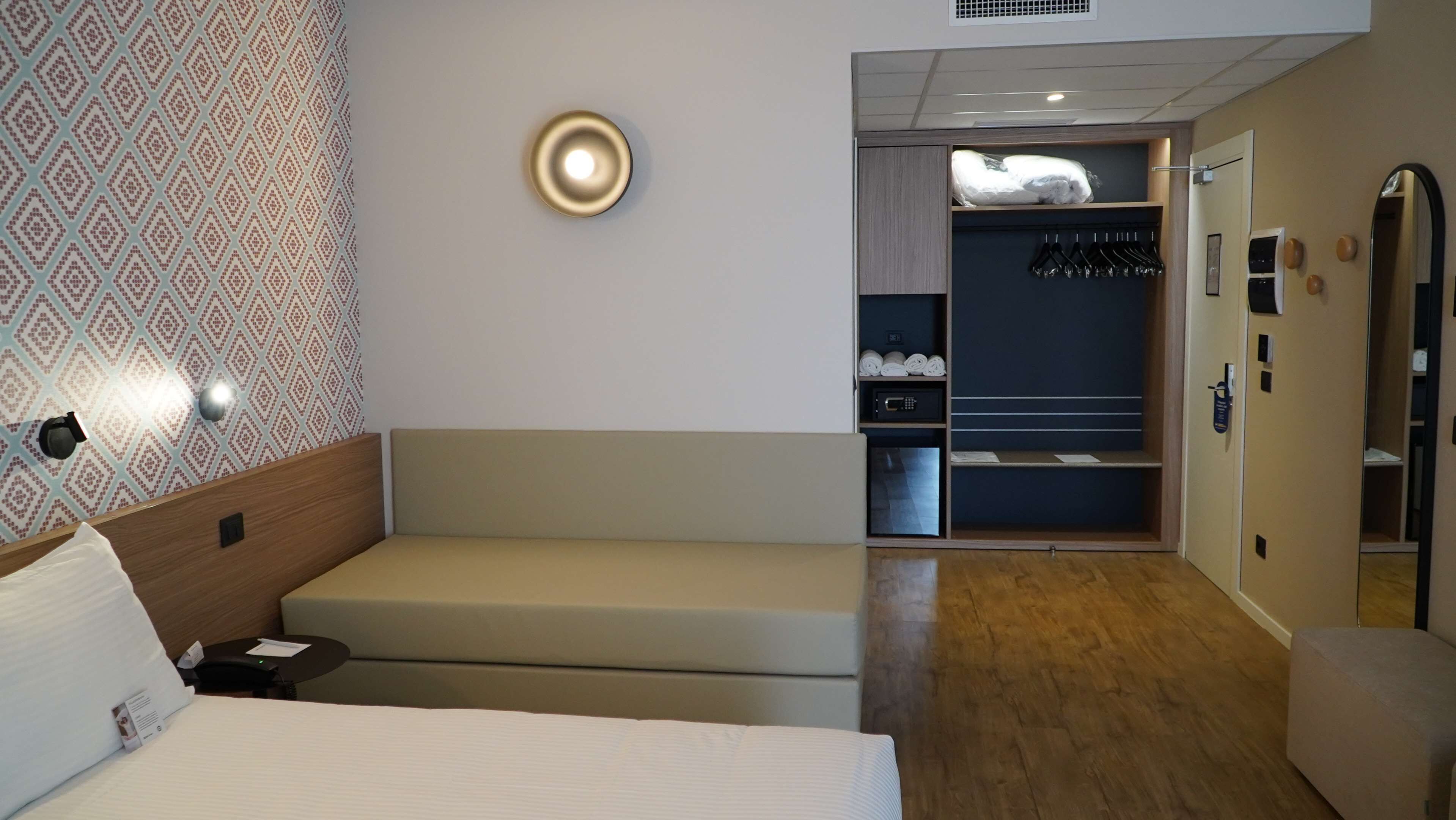 Habitación de hotel con cama, zona de estar, armario con ropa colgada y espejo.