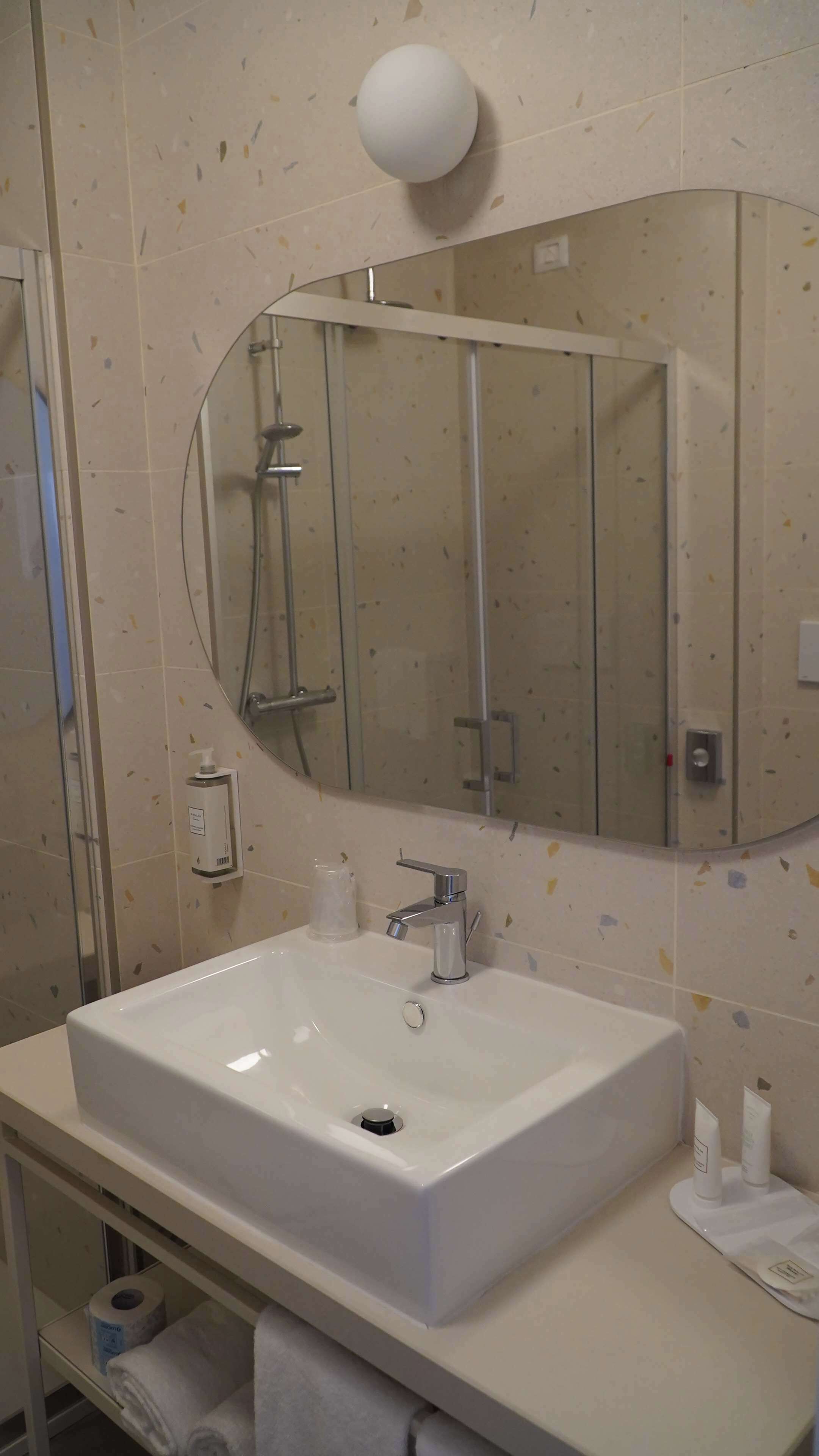 Un baño con lavamanos blanco, un espejo grande y un cabezal de ducha manual.