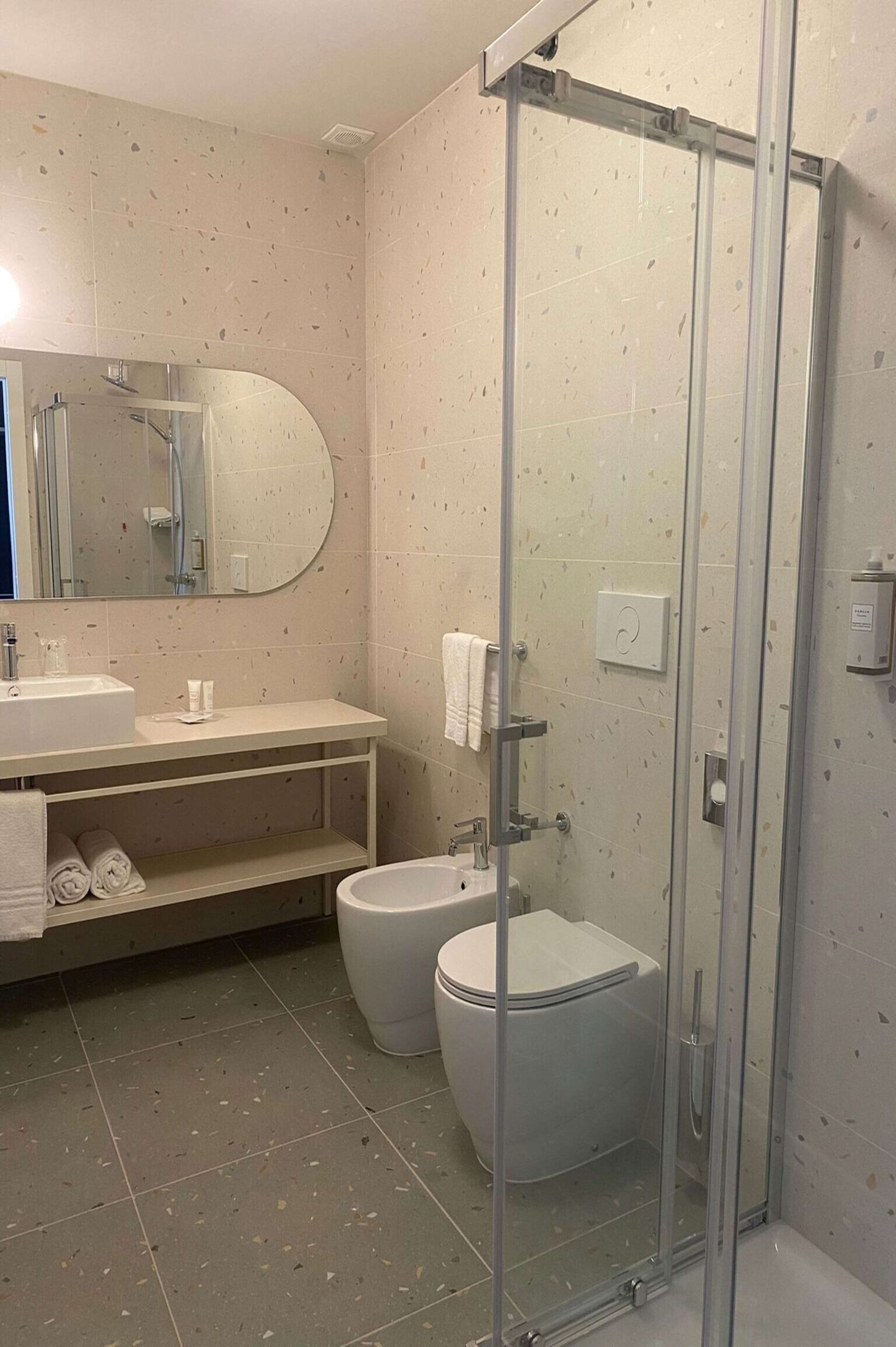 A modern bathroom with a glass-enclosed shower, a toilet, and a sink with a mirror above it.