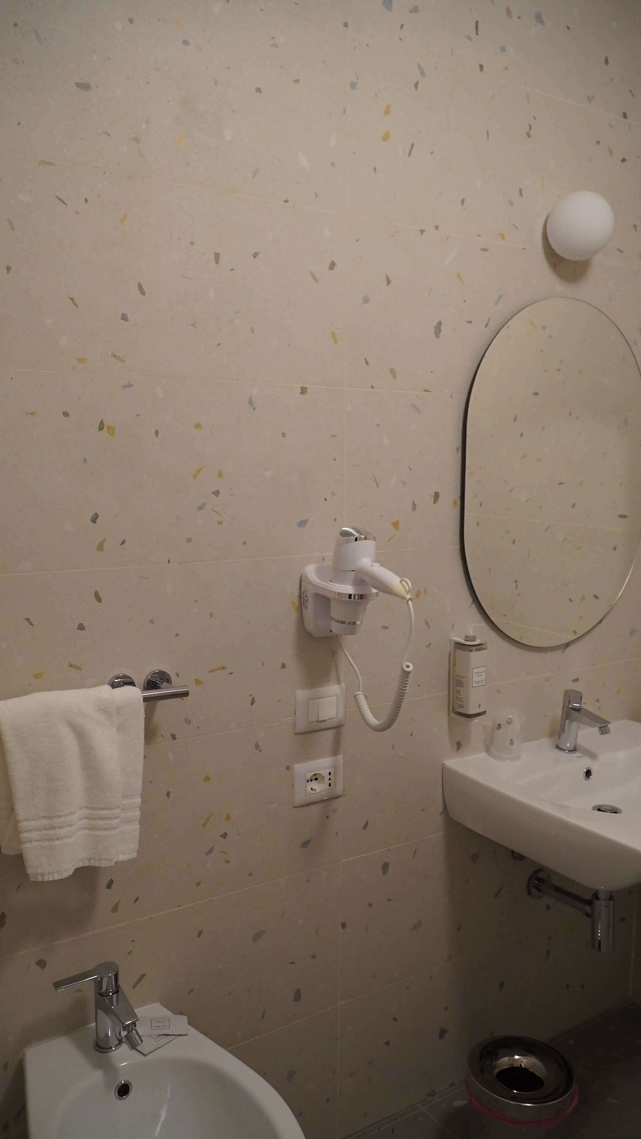 Un baño con un lavabo blanco, un espejo, un secador de pelo y una toalla colgada en un perchero.