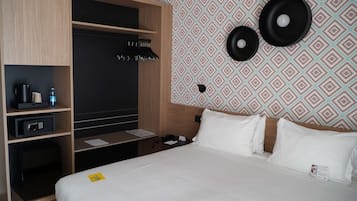 Una habitación de hotel con una cama, un escritorio con computadora, un armario y un papel tapiz estampado.