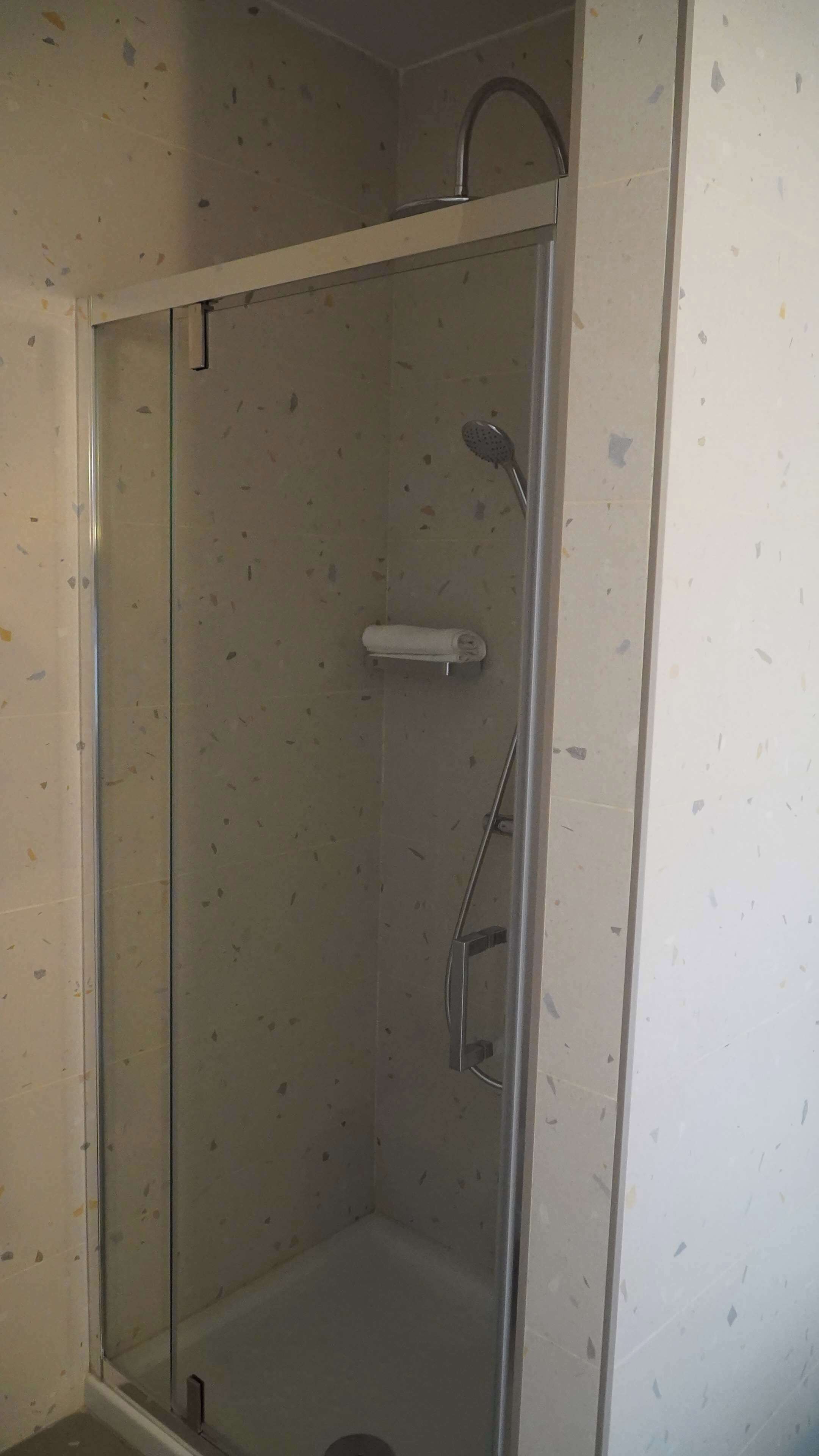 Cabina de ducha con paredes de vidrio, un cabezal de ducha de mano y un grifo de pared.