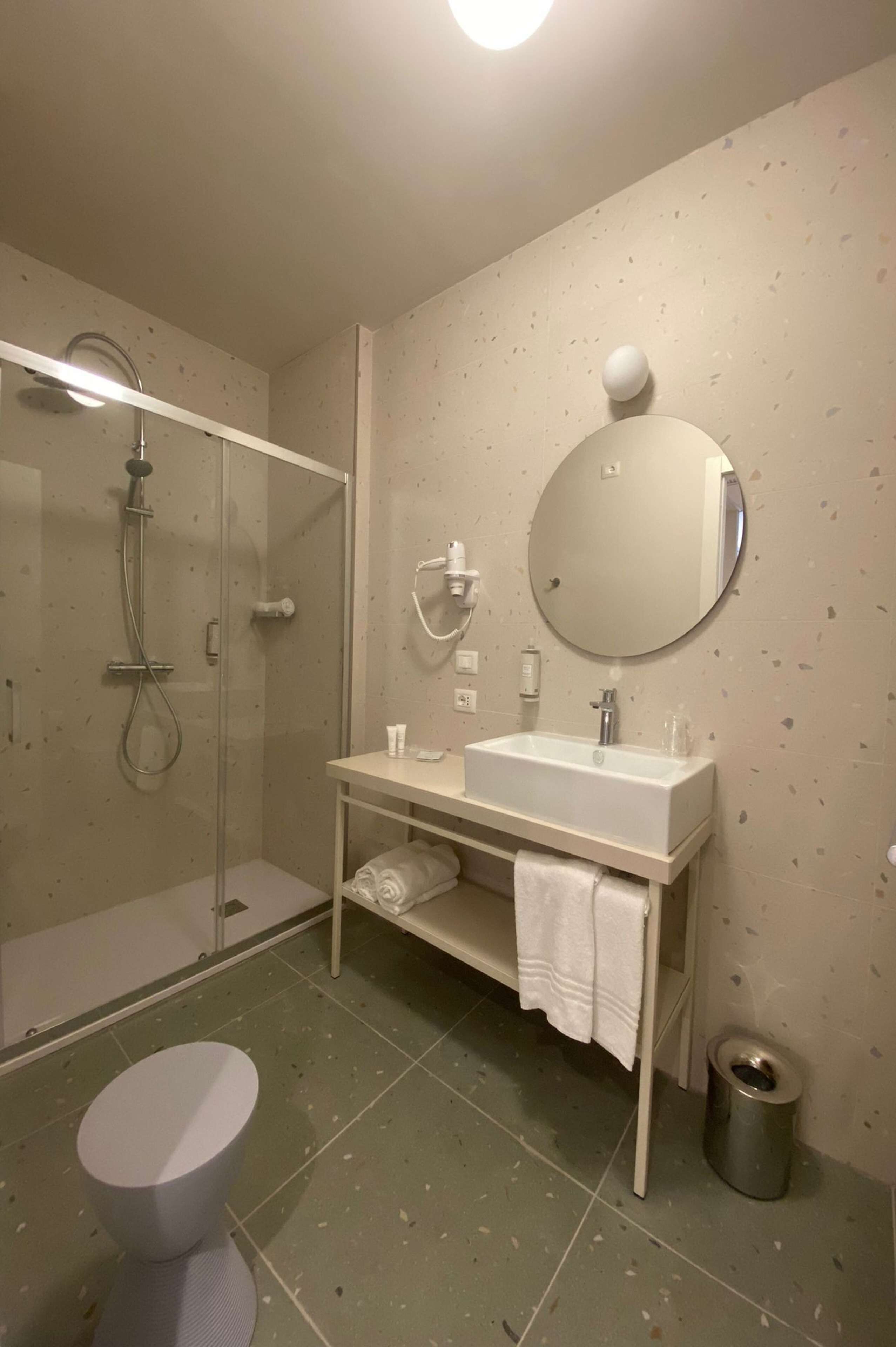 A modern bathroom with a glass-enclosed shower, a white sink with a round mirror, and a toilet.
