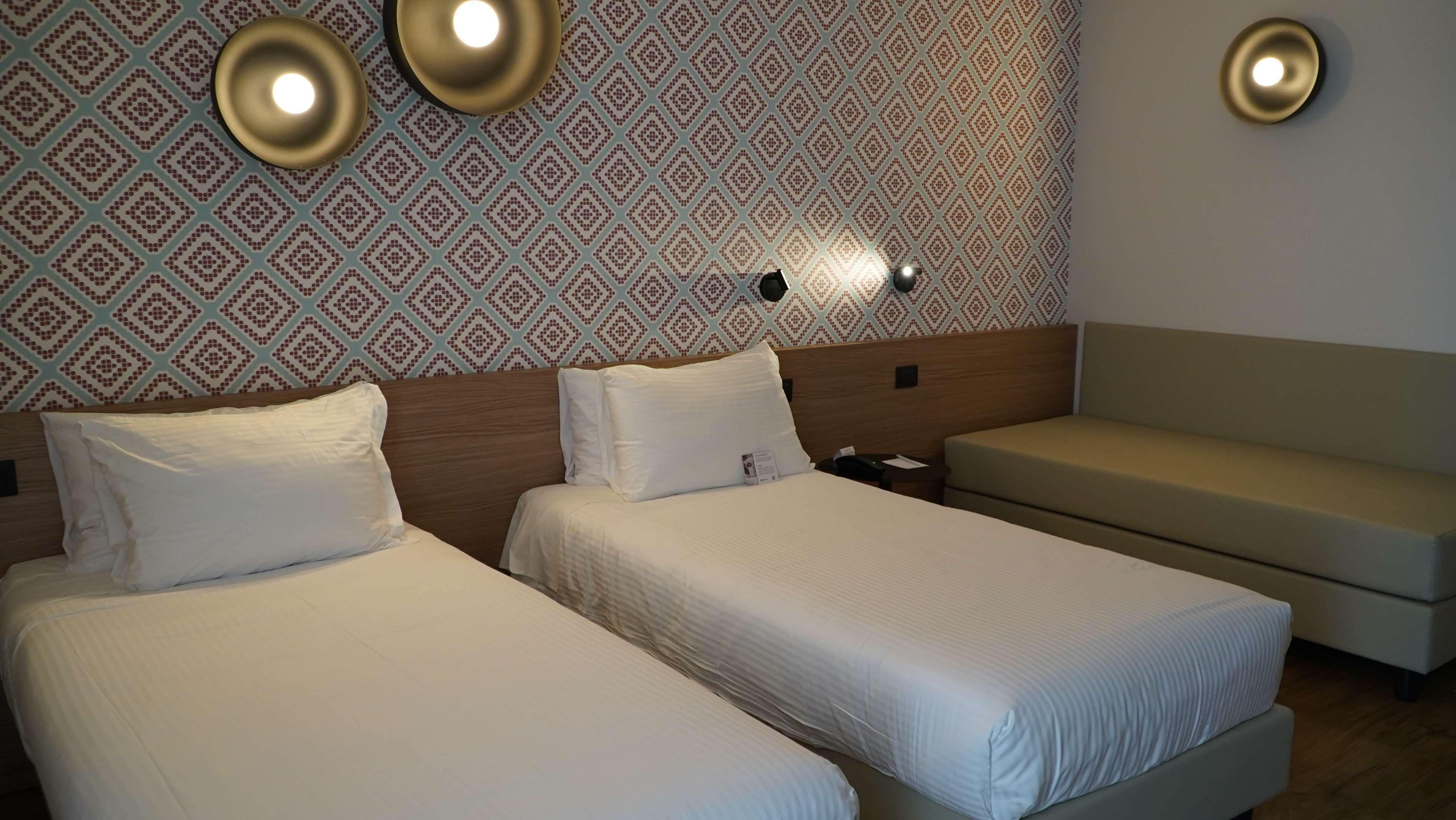 A hotel room with two beds, a sofa, and patterned wallpaper.